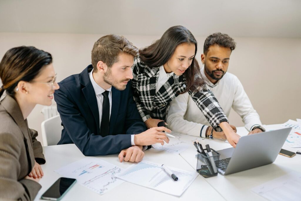 Diverse team of professionals working together on a laptop, analyzing charts and data in an office setting.